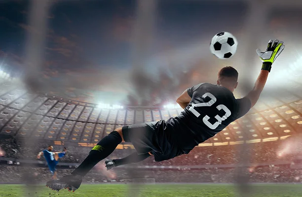 Un gardien de but de football plongeant pour arrêter un ballon dans un stade bondé, illustrant l'action spectaculaire, la performance athlétique et l'intensité du football professionnel.