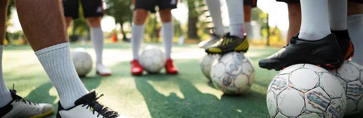 Des footballeurs debout sur un terrain d'entraînement, un ballon de football à leurs pieds, symbolisant le travail d'équipe, l'entraînement et la préparation.